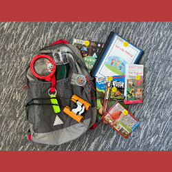 grey backpack with books nearby. magnifying glass and binoculars sit on top of backpack.