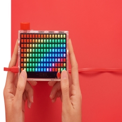 Pixel KIt with rainbows and hands holding it against a red background